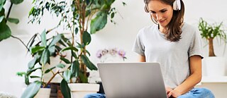 Una ragazza con un portatile e una cuffia rossa sorride mentre un gatto le passa sulla tastiera