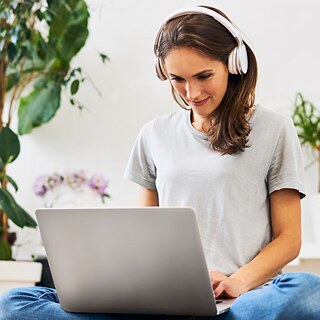 Una ragazza con un portatile e una cuffia rossa sorride mentre un gatto le passa sulla tastiera