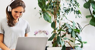 Eine junge Frau mit Laptop und rotem Kopfhörer lächelt, während eine Katze über die Tastatur geht