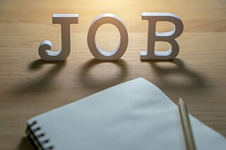 Wooden letters spell the word "Job" on a desk. In front of them lies a notepad with a pencil.