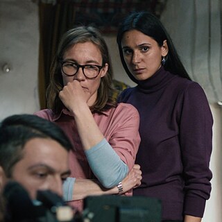 Szene aus dem Film „Im toten Winkel“: In einem Raum stehen zwei Frauen, und im Vordergrund sieht man den Kopf eines Mannes, der am Computer sitzt.