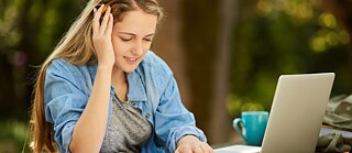 Frau lernt im Freien mit Laptop und Buch