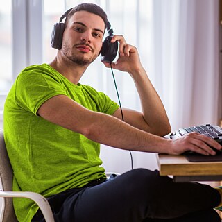 גבר צעיר עם אוזניות יושב מול מחשב נייד