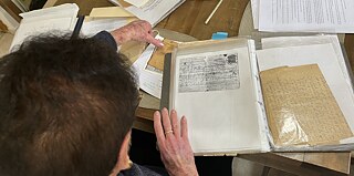 אישה יושבת ליד שולחן וממיינת מכתבים ומסמכים.
