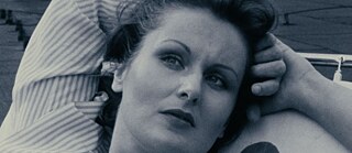 Black-and-white close-up of a white woman, looking affectionate with her arms clasped behind her head