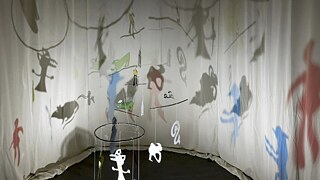 artwork by Rania Atef: Immersive installation with hanging, cut-out figures casting layered shadows on curved white walls, creating a floating, dreamlike scene of abstract creatures and forms.