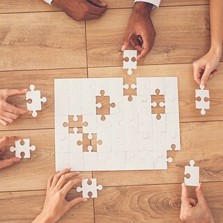 Aufnahme von oben auf einen Tisch. Mehrere Personen setzen ein Puzzle zusammen.