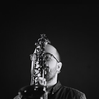 Der Musiker Mark Weschenfelder hält ein Saxofon vor seinem Gesicht.
