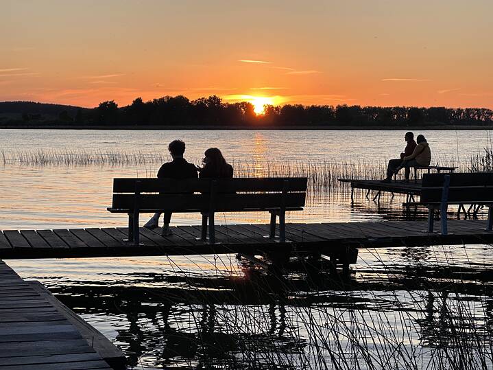 Auf einem Steg blicken Menschen auf den Sonnenuntergang am Oberuckersee.