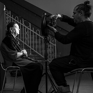 Ein schwarzweißes Bild von einer Roma Frau, die gerade vor einem schwarzen Hintergrund fotografiert wird.
