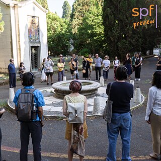Un momento dell'audiowalk collettivo "Remote Roma": i partecipanti, all'interno del Cimitero Monumentale del Verano, ascoltano in cuffia la guida di una voce artificiale.