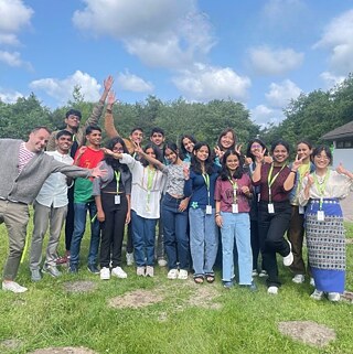 Group of PASCH students standing outdoors, wearing name badges and posing together in front of a green background.