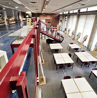 Veduta interna della biblioteca, con scala tra il livello superiore e inferiore e postazioni di lavoro per gli utenti.