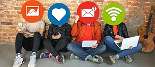 Vier Personen sitzen am Boden vor einer Wand und verdecken ihre Gesichter hinter runden Schildern.