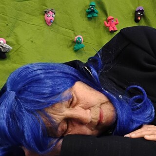 Patricia London liegt in einer blauen Perücke auf den Boden