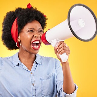 Frau, Megafon und Protest; Stimme, Nachrichten, Rundfunk oder Durchsage; Faust und gelber Hintergrund. Wütender Afrikaner, Student oder Redner in einer Position der Macht, Führung und Aufmerksamkeit oder Gerechtigkeit in einem Studio