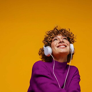 Ein junge Frau hört Musik über Kopfhörer und lächelt.