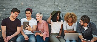 Gruppe junger Erwachsener, lachend mit Tablets und Laptops.