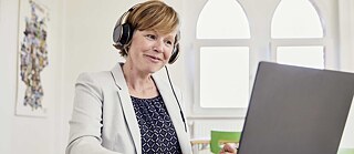 Eine Lehrkraft arbeitet konzentriert am Laptop und trägt Kopfhörer. Sie lächelt.
