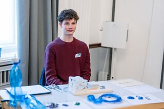 Finalist sitzt an einem Tisch vor seinem Experiment.