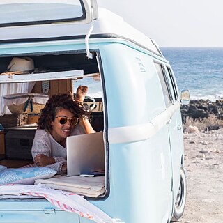 Eine junge Frau am Laptop in einem Wohnmobil am Strand