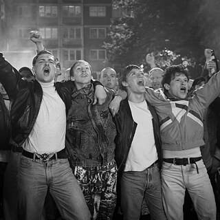 Several young men throw their arms around each other’s shoulders, shouting loudly.