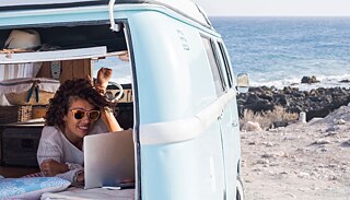 Eine junge Frau am Laptop in einem Wohnmobil am Strand