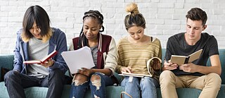 Mehrere junge Schüler sitzen nebeneinander auf einem Sofa und lesen. Die Bilder der Serie "JUNGE LERNENDE" zeigen Gruppen von jungen Lernenden – Kinder und Jugendliche -, die Spaß an Bildung, Lernen und an der deutsche Sprache vermitteln sollen.