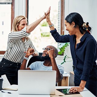 Eine Gruppe junger Leute in einem Büro jubeln und klatschen sich ab.