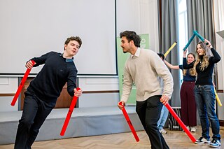 Jugendliche laufen im Kreis, sie halten rote Stäbe in der Hand.
