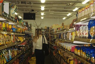 Ulička supermarketu Krakus. Zákazníčka s nákupným košíkom prechádza pomedzi regály preplnené potravinami zo strednej a východnej Európy.