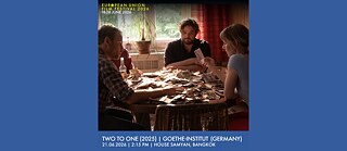 Poster des European Union Film Festival 2026, das eine Szene mit drei Personen zeigt, die um einen Tisch in einem Raum sitzen, in den Sonnenlicht durch ein Fenster fällt. In der Mitte des Tisches liegen zahlreiche verstreute Geldscheine.
