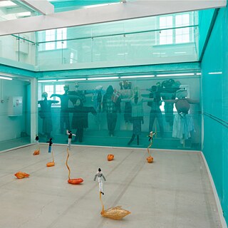 Billede fra installationen i Viborg Kunsthal. Bag blåt glas ses en række fugleskræmsler, i forgrunden mindre figurer på gulvet.