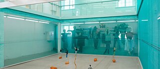 Billede fra installationen i Viborg Kunsthal. Bag blåt glas ses en række fugleskræmsler, i forgrunden mindre figurer på gulvet.