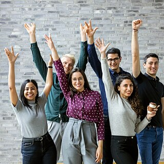 Lehrkräfte heben jubelnd die Hände, lachen und feiern ihren Erfolg. 