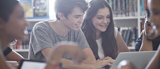 Junge Leute studieren mit Laptop an einem Tisch in einer Bibliothek 