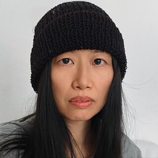 Portrait of Zhou Fei wearing a black knit cap against a simple light background.