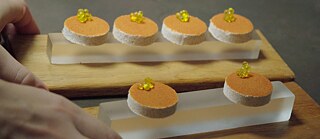 Nahaufnahme eines Desserts bestehend aus organgefarbenen runden Elementen auf einer Holzplatte
