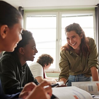 A smiling German teacher explains German grammar to her students.