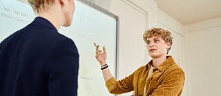 Ein Schüler bearbeitet eine Grammatikaufgabe mit seiner Deutschlehrerin an der digitalen Tafel.​