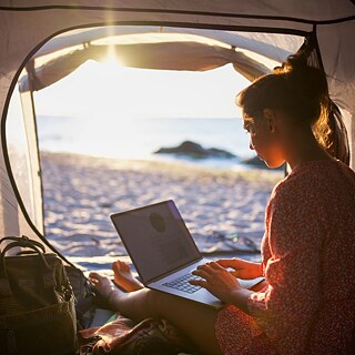 Eine junge Frau am Laptop in einem Wohnmobil am Strand