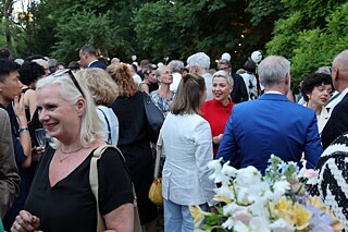 Unterschiedliche Menschen stehen draußen in einem Garten und unterhalten sich angeregt miteinander. 