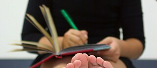 Jugendliche sitzt auf dem Fußboden und schreibt in eine Heft.