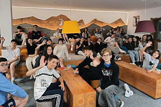 Jugendliche in einem modern gestalteten Aufenthaltsraum grüßen in die Kamera.