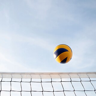 Ein Volleyball in der Luft, am Bildrand unten sieht man das Netz.
