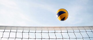Ein Volleyball in der Luft, am Bildrand unten sieht man das Netz.
