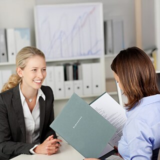 Two people sit face to face discussing documents.