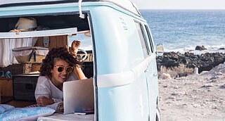Una ragazza sorridente con PC portatile in un camper in spiaggia