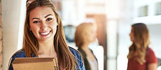 Eine junge, lächelnde Frau mit Büchern und Heften