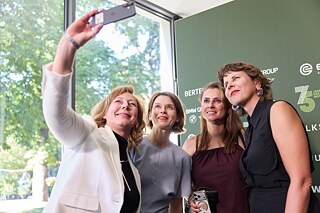 Vier Frauen stehen vor einer Fotowand und machen gemeinsam ein Selfie. 